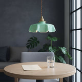Green pendant light hanging above a wooden table with a glass of water and a piece of paper in a room with a gray sofa and plants.