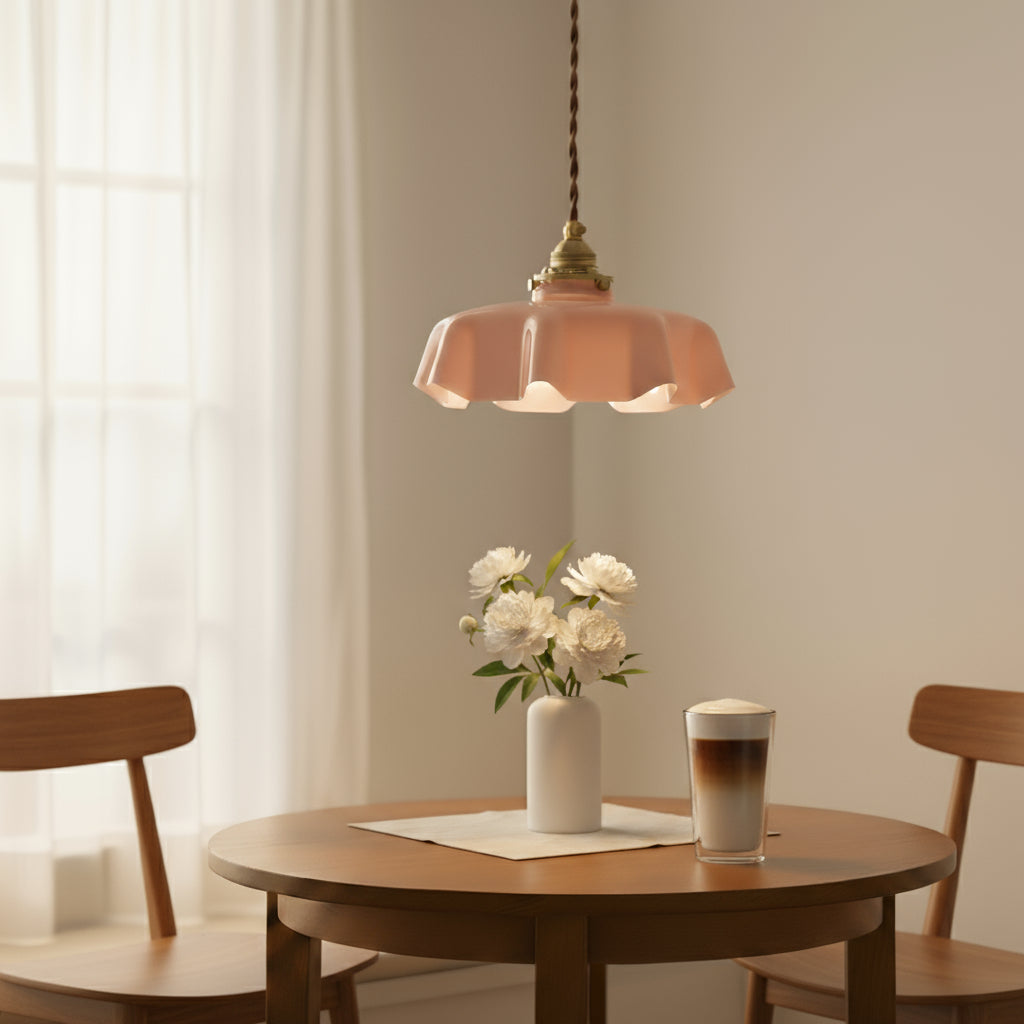 Pink pendant light above a wooden table with a vase of flowers and a coffee cup.