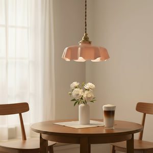 Pink pendant light above a wooden table with a vase of flowers and a coffee cup.