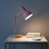 Pink desk lamp on a marble surface with books and a bowl against a blue wall.