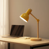 Yellow desk lamp on a wooden desk with a laptop and notebook.