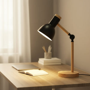 Black desk lamp on a wooden desk with a notebook and pen holder in a softly lit room.