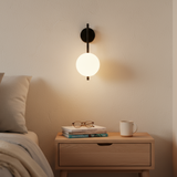 Bedroom scene with a nightstand, lamp, and books against a neutral wall.