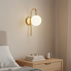 Wall-mounted lamp on a neutral wall above a wooden nightstand with books and a mug.