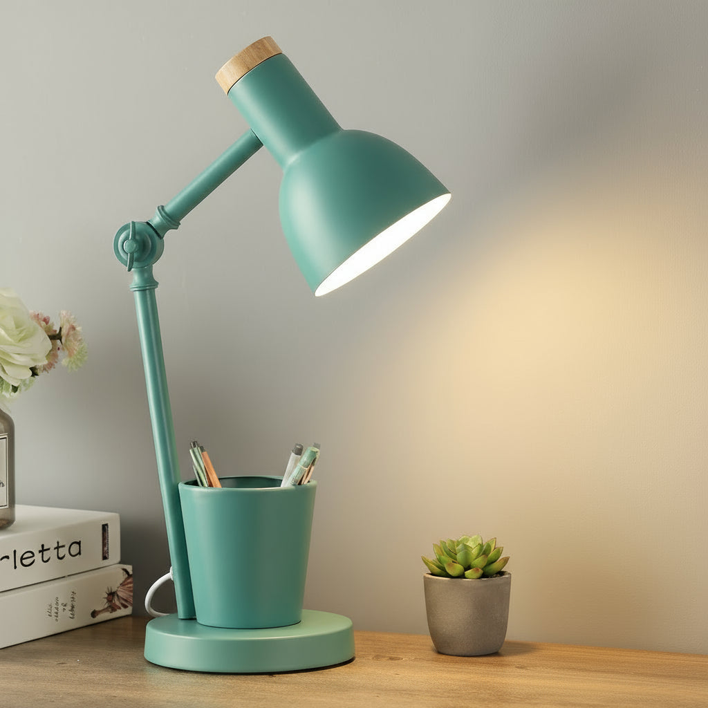 Teal desk lamp with a cup holder on a wooden surface, with books and a plant in the background.