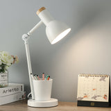 White desk lamp on a wooden surface with a cup of pens, books, and a calendar in the background.