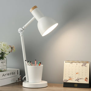 White desk lamp on a wooden surface with a cup of pens, books, and a calendar in the background.