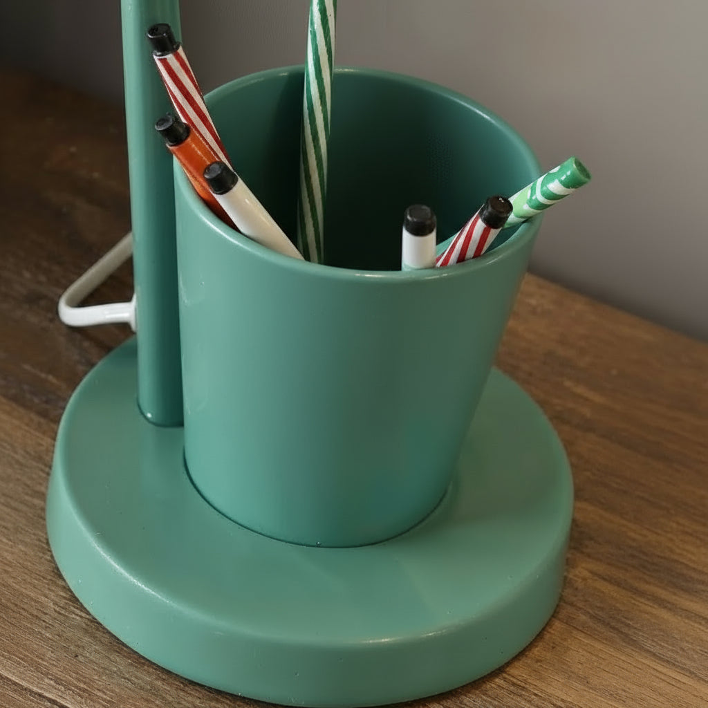 Green pen holder with pens on a wooden surface