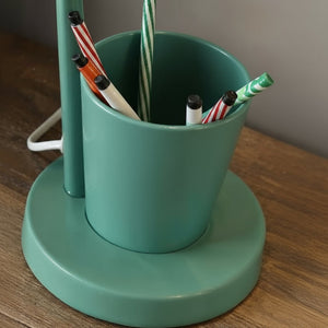 Green pen holder with pens on a wooden surface