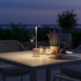 Outdoor setting with a table, candles, and a lamp at dusk.