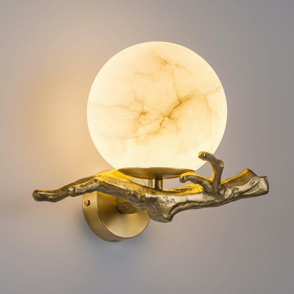 Wall-mounted light fixture with a gold branch-like design and marble-textured shade on a gray background