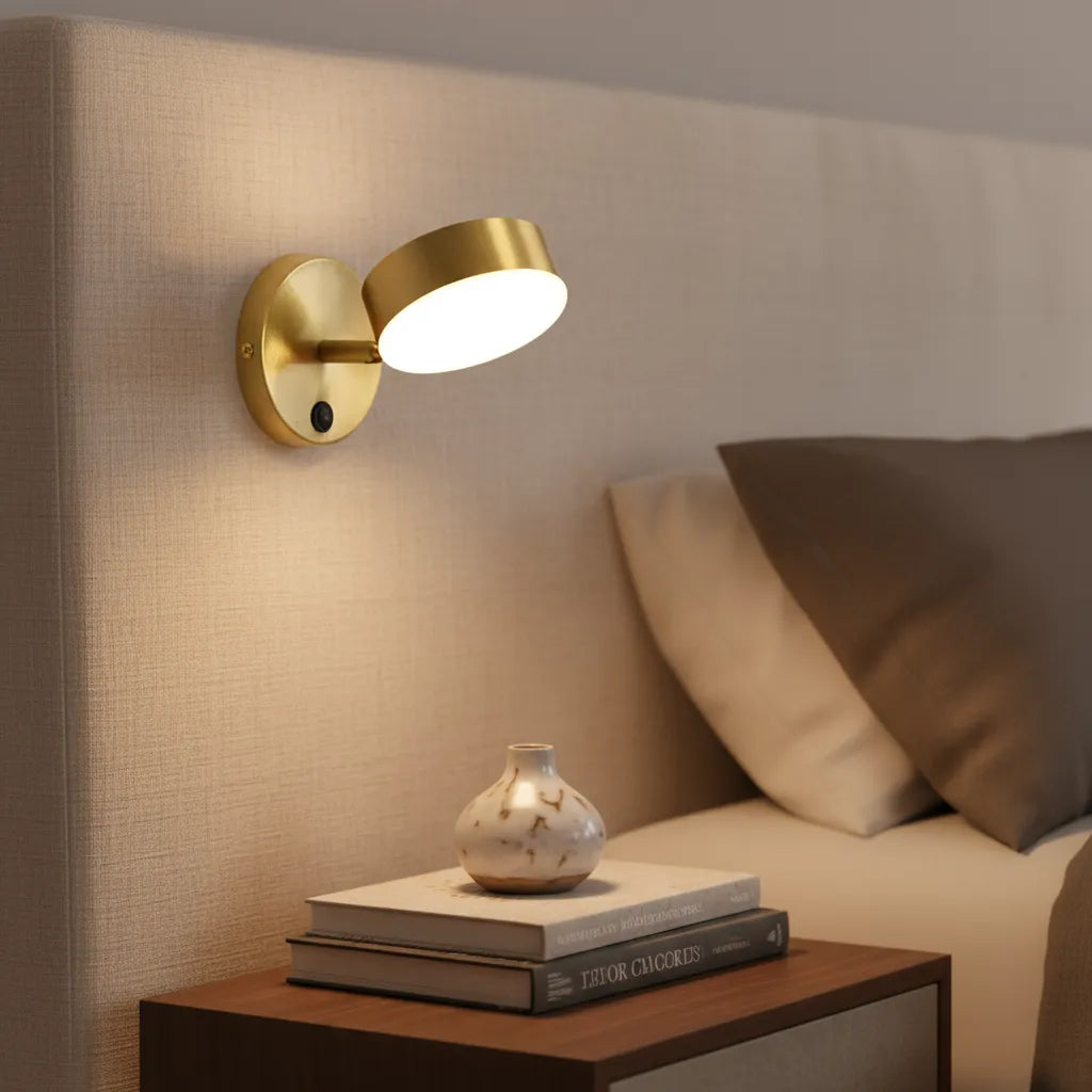 Gold wall sconce on a beige wall with books and a vase on a wooden nightstand.